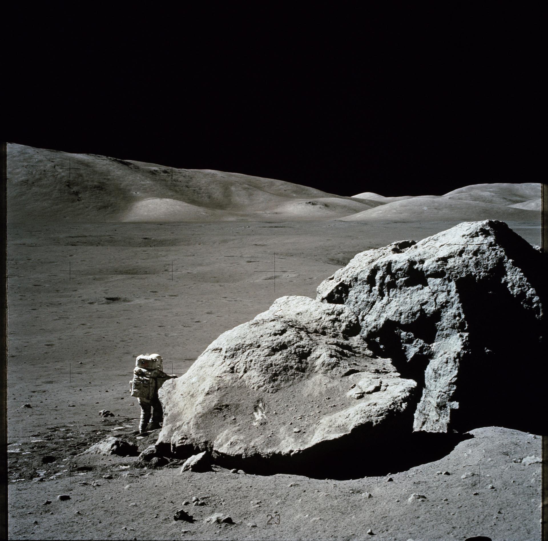 An astronaut working beside a boulder on the lunar surface